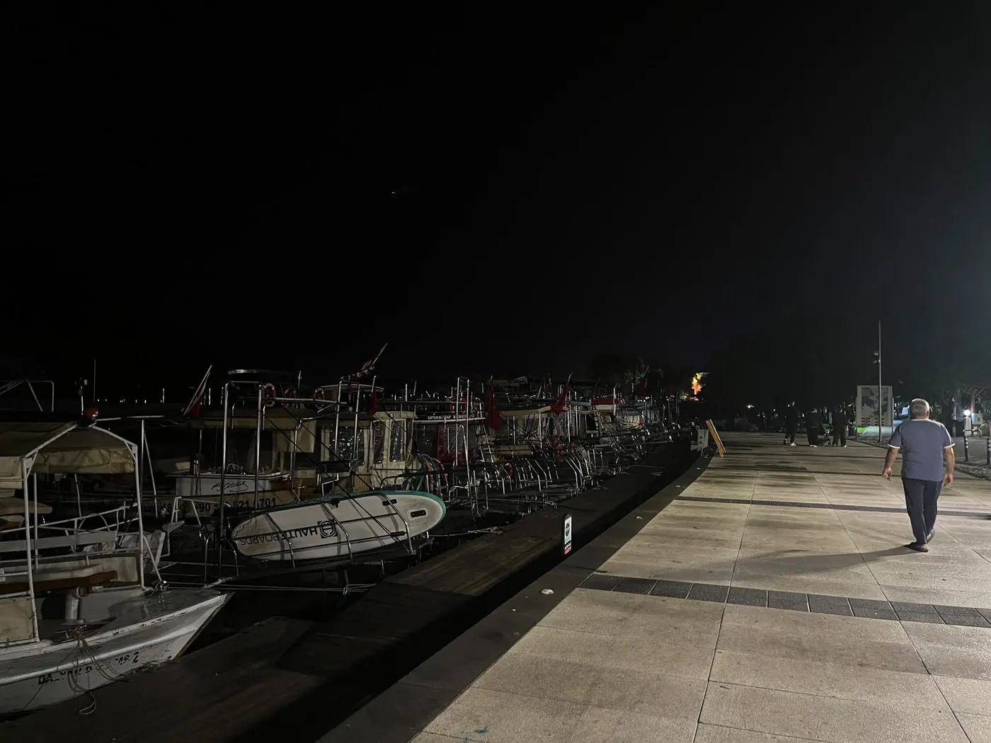 Wooden boats moored along the quay at night, a man walking the promenade Wooden boats moored along the quay at night, a man walking the promenade