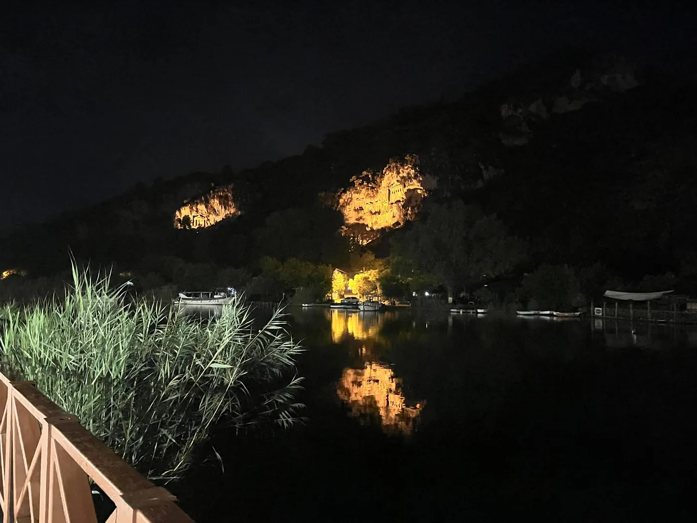 Nehir kenarındaki korkuluktan aydınlatılmış kaya mezarları ve suya düşen yansıması