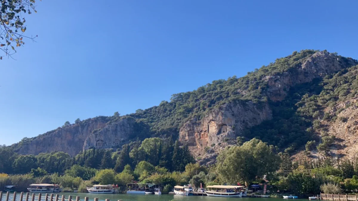 Boats at the Dalyan quay with the rock tombs rising behind them