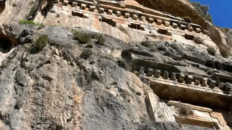 A columned tomb façade close up, with a rough-cut chamber beside it A columned tomb façade close up, with a rough-cut chamber beside it